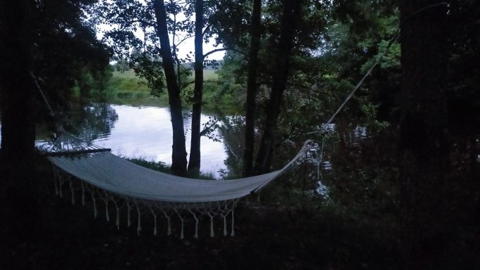 Hangmat tussen bomen bij een rustige rivier in de schemering.