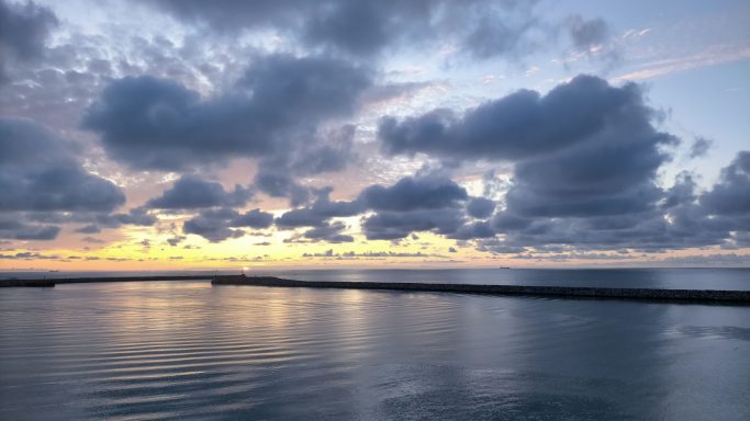 Zonsondergang boven kalm water met wolken in de lucht.