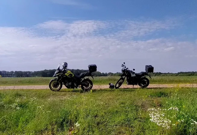 Twee motorfietsen staan op een onverharde weg omringd door gras en bloemen.