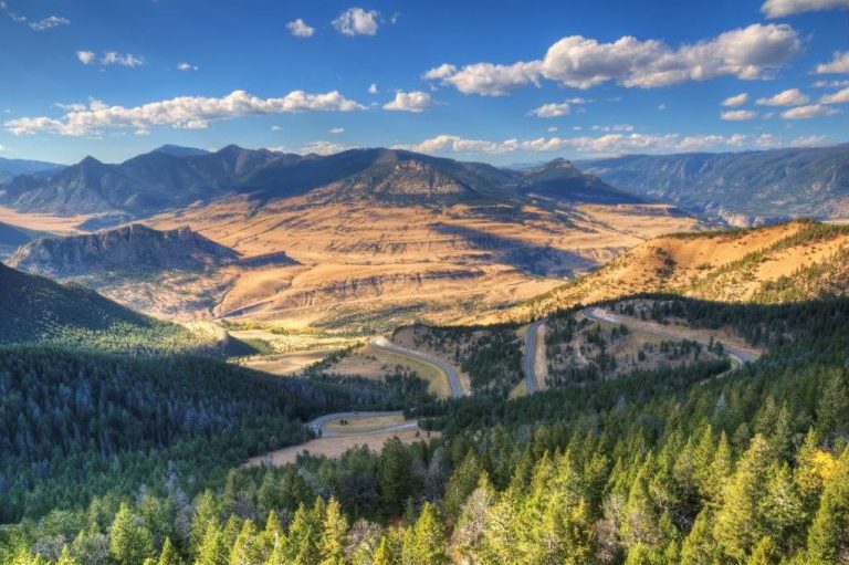 Uitzicht op een bergachtig landschap met valleien en bossen onder een blauwe lucht.