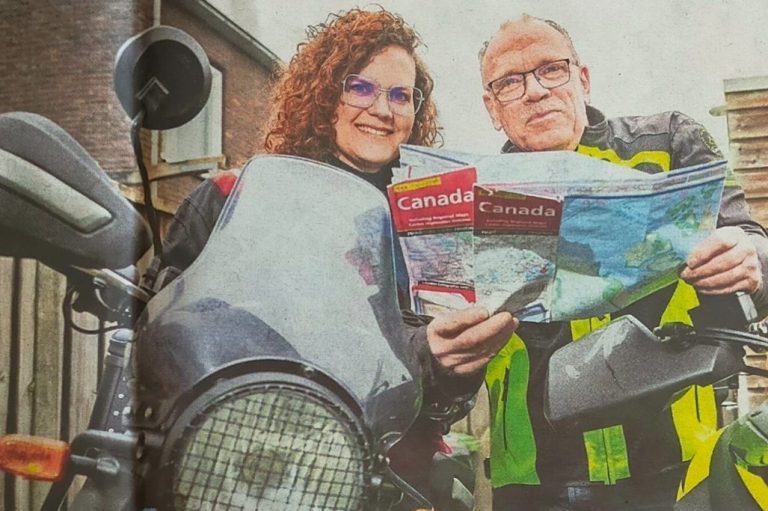 Een rechte weg leidt naar een besneeuwde berg met dennenbomen aan de zijkanten.